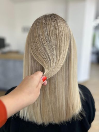 Hinterkopf einer Person mit glattem, blondem Haar, das sanft gehalten wird.
